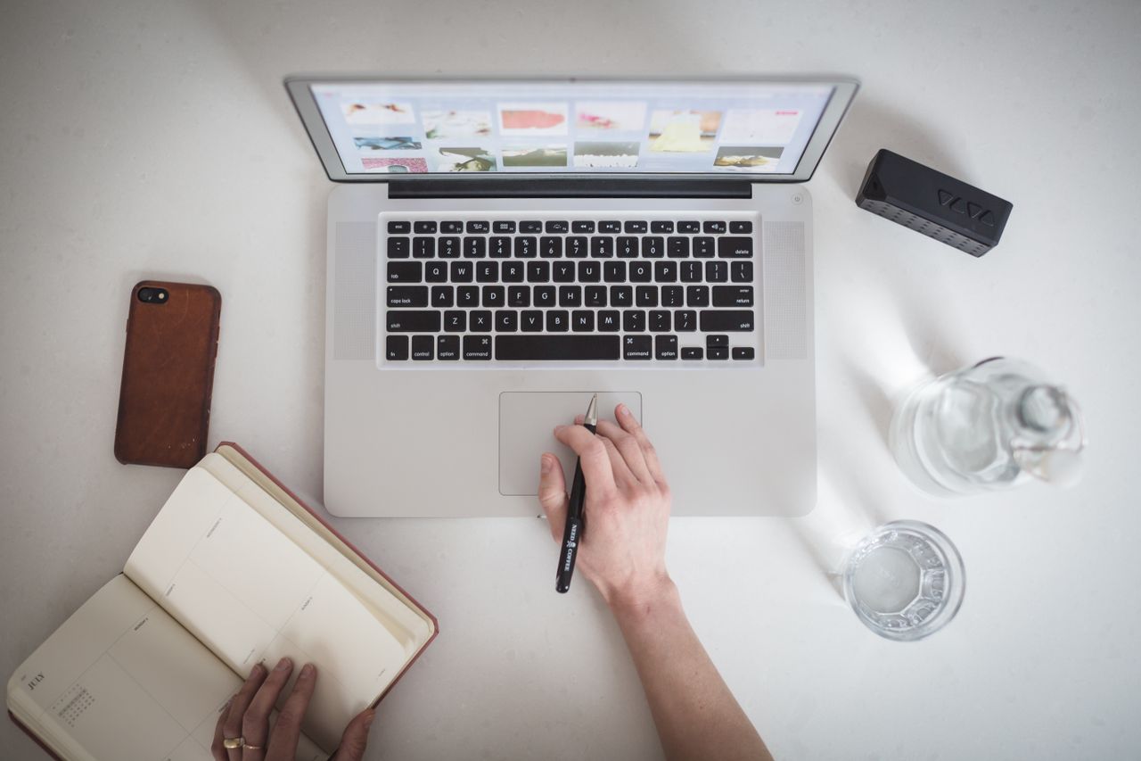 Top-down view of a workspace featuring a laptop, notebook, smartphone, and glass of water, ideal for remote work.